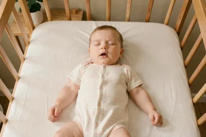 Bébé de 6 mois dormant sans gigoteuse dans un lit à barreaux en bois avec un body rayé pastel